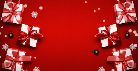 Surprise box. White gifts with scarlet bow, red balls and sparkling lights in xmas decoration on reddish background for greeting card. Flat lay, top view, copy space.