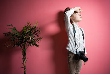 A little girl of European appearance with a camera on a pink background. Self-isolation. 