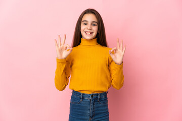 Little girl isolated on pink background showing ok sign with two hands