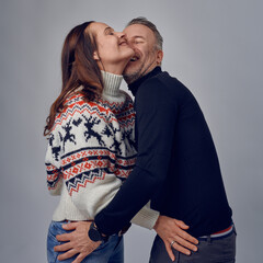 Adult man kissing his happy laughing wife. Loving couple in warm sweaters posing for family portrait. Winter holidays photoshoot concept in studio