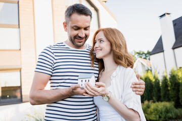 Smiling husband with statuette of house hugging wife on blurred background