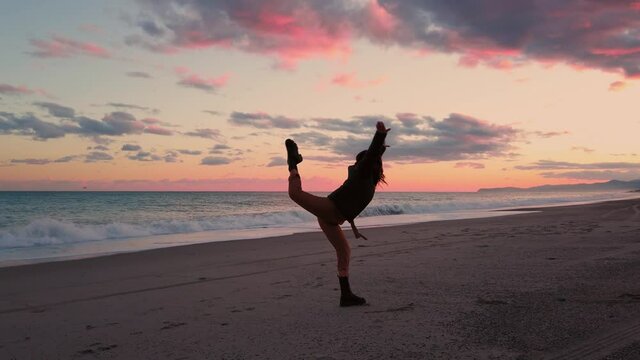 Ragazza con stivali anfibi nero balla sulla spiaggia al tramonto