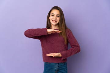 Little girl isolated on purple background holding copyspace imaginary on the palm to insert an ad