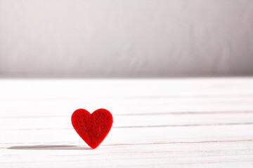 Fototapeta premium Red felted heart on white wooden background. Valentine's day. Romance greeting card. Copy space. Minimalism.