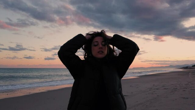 Ragazza danza in spiaggia all'alba con il cappotto nero