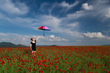 Young beautiful woman with multicolored  umbrella in poppy field. 