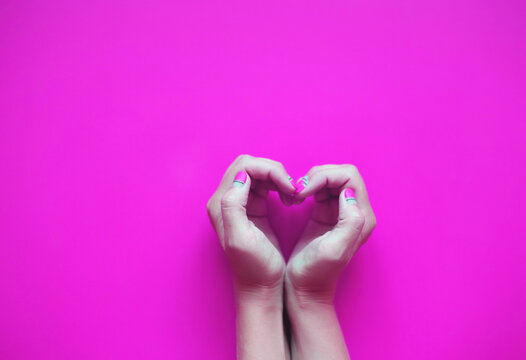 hands in the shape of a heart on a pink background