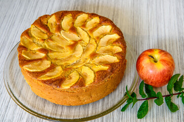 Torta de manzana sobre plato de vidrio con manzana roja y rama verde al lado 