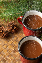 Aerial view of two red cups with chocolate, with falling sugar, on a table braided with branches and pine cones, vertically, with copy space