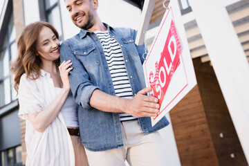 Low angle view of smiling couple holding sign with sold lettering near house