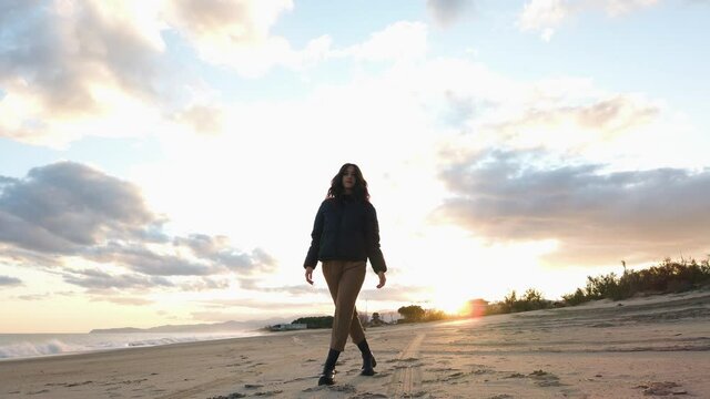 Bella ragazza con stivali balla sulla spiaggia al tramonto in inverno