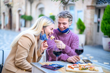 Beautiful happy couple are feeding each other in the restaurant in covid-19 time - Young rasta man is feeding her girlfriend - Happy woman eat lifestyle at bar concept