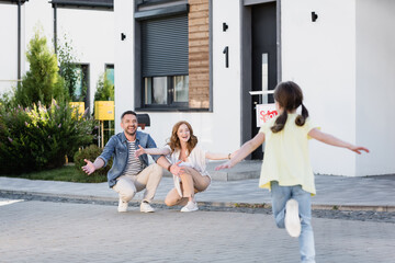 Happy parents squatting and looking at blurred daughter running on foreground