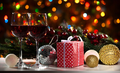 Glasses of wine and Christmas gift and balls on the background of Christmas lights and Holly red berries