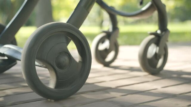 Wheels of baby stroller rolling in sunlight along alley in summer park. Baby carriage outdoors on sunny day. Motherhood and childhood concept.
