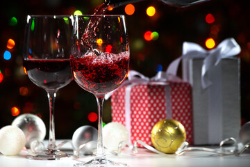 Beautiful splash of red wine in glasses on the background of Christmas lights and Christmas gifts and balls