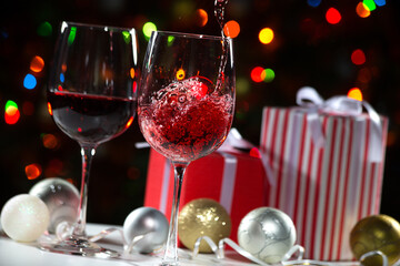 Beautiful splash of red wine in glasses on the background of Christmas lights and Christmas gifts and balls