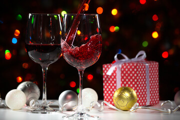 Beautiful splash of red wine in glasses on the background of Christmas lights and Christmas gifts and balls