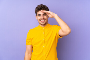 Caucasian man isolated on purple background saluting with hand with happy expression