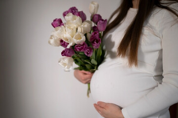 Pregnant girl in a white dress holding a bouquet of tulips. 
Gifts and waiting time for the baby.