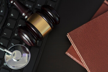 Top view of Judge's gavel and medical stethoscope on computer keyboard and books on woodeb table