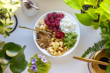 Fresh fruit salad with muesli, cottage cheese, raspberries, banana, apple, kiwi in a plate with a golden spoon for a healthy breakfast. Flat lay. Isolated white background banner.