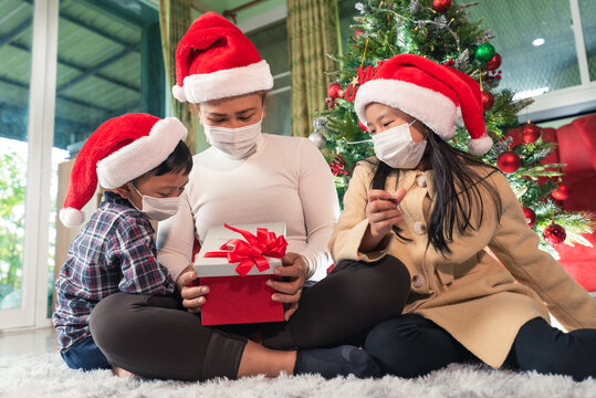 the family wearing the protective mask and opening gift boxes during the Christmas festival celebration.