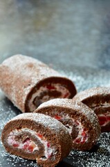 Homemade chocolate sponge cake roll with strawberries and cream filling, powdered sugar on top, on a slate plate, copy space