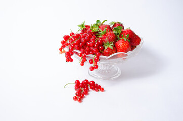 Vase on a long leg with fruit with strawberries and red currants and several berries on a white background.