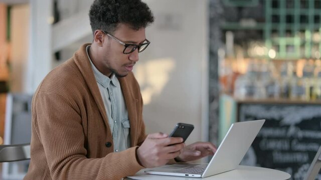 African Man with Laptop using Smartphone in Cafe