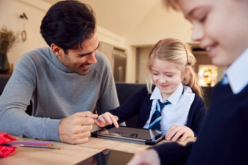 Father Helping Children Using Digital Tablets Wearing School Uniform With Homework At Table