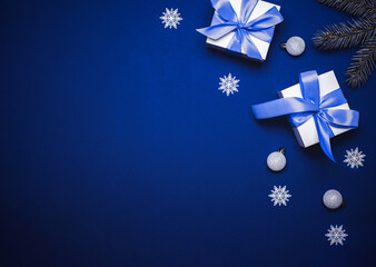 Christmas ornaments. White gift box with cyan ribbon, New Year balls and winter tree in xmas composition on dark blue background for greeting card. Decoration, copy space for your text.