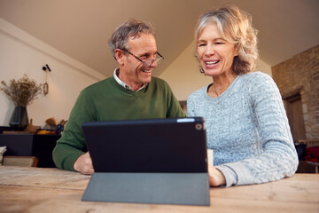 Retired Senior Couple At Home Buying Products Or Services Online Using Digital Tablet