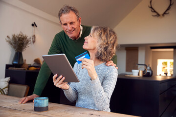 Retired Senior Couple At Home Buying Products Or Services Online With Digital Tablet And Credit Card