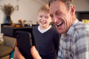 Grandson With Grandfather Smiling And Taking Selfie On Mobile Phone At Home