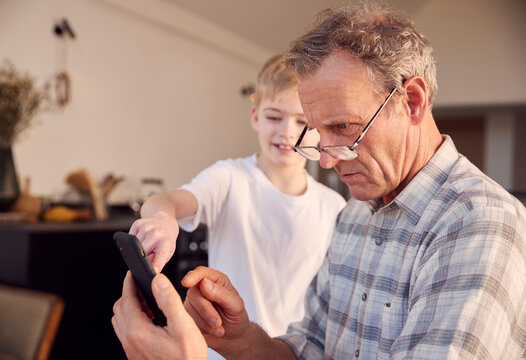 Grandson Showing Grandfather How To Solve Problem And Use Mobile Phone At Home