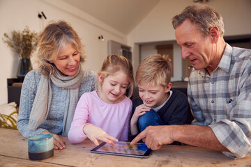 Grandchildren With Grandparents Playing On Digital Tablet At Home Together