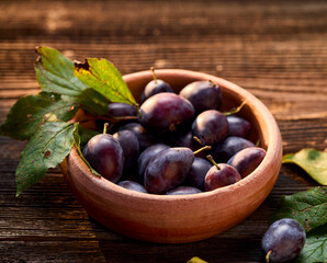 Fresh plums in a clay rustic bowl on a wooden table, close up view