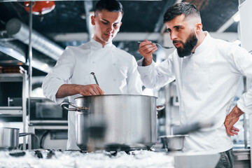 With help from other employee. Chef in white uniform cooking food at kitchen. Busy day at work