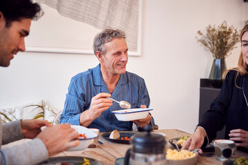 Multi-Generation Family Sitting Around Table At Home In Pyjamas Enjoying Brunch Together