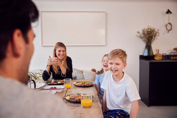 Family Sitting Around Table At Home In Pyjamas Enjoying Brunch Together