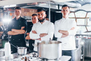 Group of people in white uniform standing together at kitchen. Cooking food