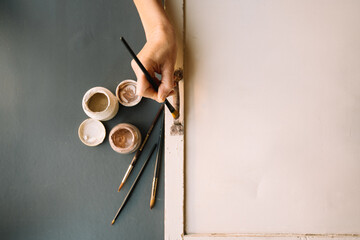 mid-aged woman holding paintbrush and repairing old furniture painting wooden. home hobbies during quarantine, lockdown. paint jars and brushes. diy projects.