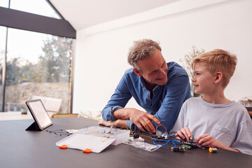 Grandson With Grandfather Assembling Electronic Components To Build Robot Together At Home