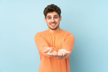 Caucasian man isolated on blue background holding copyspace imaginary on the palm to insert an ad