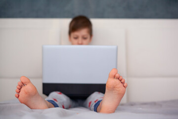 Cute little boy child Laying on the bed at home looking at laptop computer screen. Selective focus on bare foot. © Volha Zaitsava
