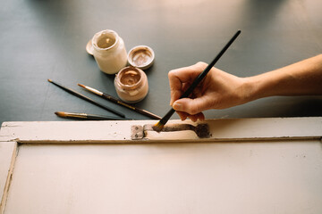 mid-aged woman holding paintbrush and repairing old furniture painting wooden. home hobbies during quarantine, lockdown. paint jars and brushes. diy projects.