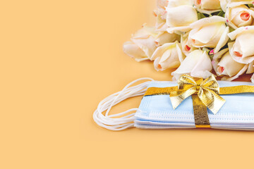 A bouquet of roses and protective medical masks with a Golden ribbon and bow on a pastel background. Copy space, flat lay. Gift for birthday, Wedding, Mother's Day, Valentine's day during pandemic.
