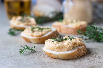 Homemade pate, spread or mousse in glass jar with sliced bread and herbs, light concrete background.