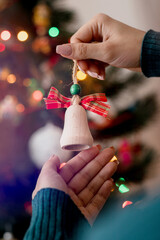 Woman holding christmas tree wooden toy in her hands and hanging it on the Christmas fir tree. Winter holidays lights and garlands. Festive mood concept.
